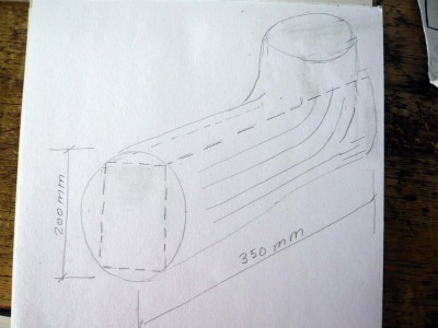 Toca ahora ponerse con los apóstoles de estribor. Para esto parto de un taco de madera cuyas vetas sigan las formas redondeadas de estos elementos. Este taco lo saqué de una horquilla de cerezo de las dimensiones que os pongo en el dibujo y en él, con trazo discontinuo, quiero representar los cortes que hice con el serrucho; los trazos continuos en el lateral del tronco indican la dirección de la veta de la madera.