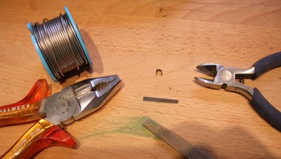 Confección de los herrajes del timón.<br />Alicates, estaño, lima, lámina de metal.<br />En el centro, la lámina ya doblada y cortada.