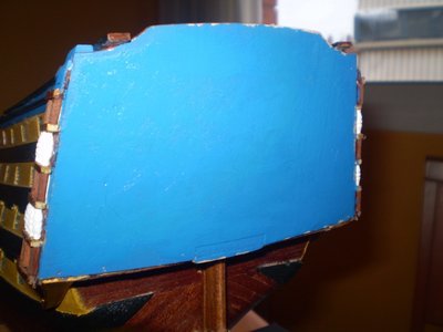Mientras la peineta va cogiendo forma, Puliremos con papel de lija de grano fino el espejo de popa. Después, con pintura del mismo color azul que utilizamos para los jardines laterales, pintaremos el espejo. Lo reservaremos hasta que la pintura se seque.