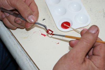 Con unas pinzas cojemos los marcos de las troneras y los pintamos de rojo junto con las portas.