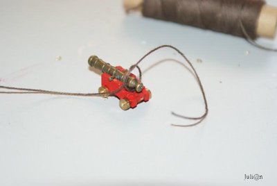 Para elaborar la braga de retroceso del cañón, cogemos un trozo de hilo marrón de 0,25 de grosor y, cortamos un trozo de hilo de aproximadamente 150 mm de longitud. Realizamos un nudo simple que abrace el cascabel del cañón, tal como muestra la fotografía, y fijamos el nudo con un poco de pegamento. Realizamos las mismas operaciones con los otros 27 cañones.