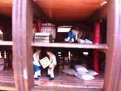 Interior de las bodegas. Con barriles, cajas, materiales, suministros, todo tipo provisiones y hombrecillos.