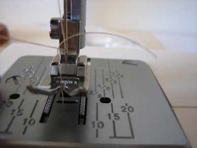 girando manualmente hacia nosotros la palanca o rueda central que se suele ubicar a la derecha de la máquina, hacemos bajar la aguja hasta abajo del todo, cuando sube nos saca el hilo inferior enganchado, el cual estiramos un poco para que sobresalga unos