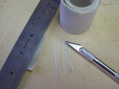 POR OTRO LADO CORTO UN POCO DE CINTA DE LA CUAL MEDIANTE CUTTER CORTO TIRITAS DE LA MEDIDA INDICADA PARA HACER LAS FAJAS.